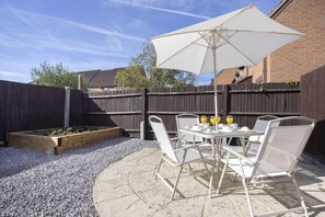Une terrasse avec une table et des chaises, un parasol et un parterre de fleurs.