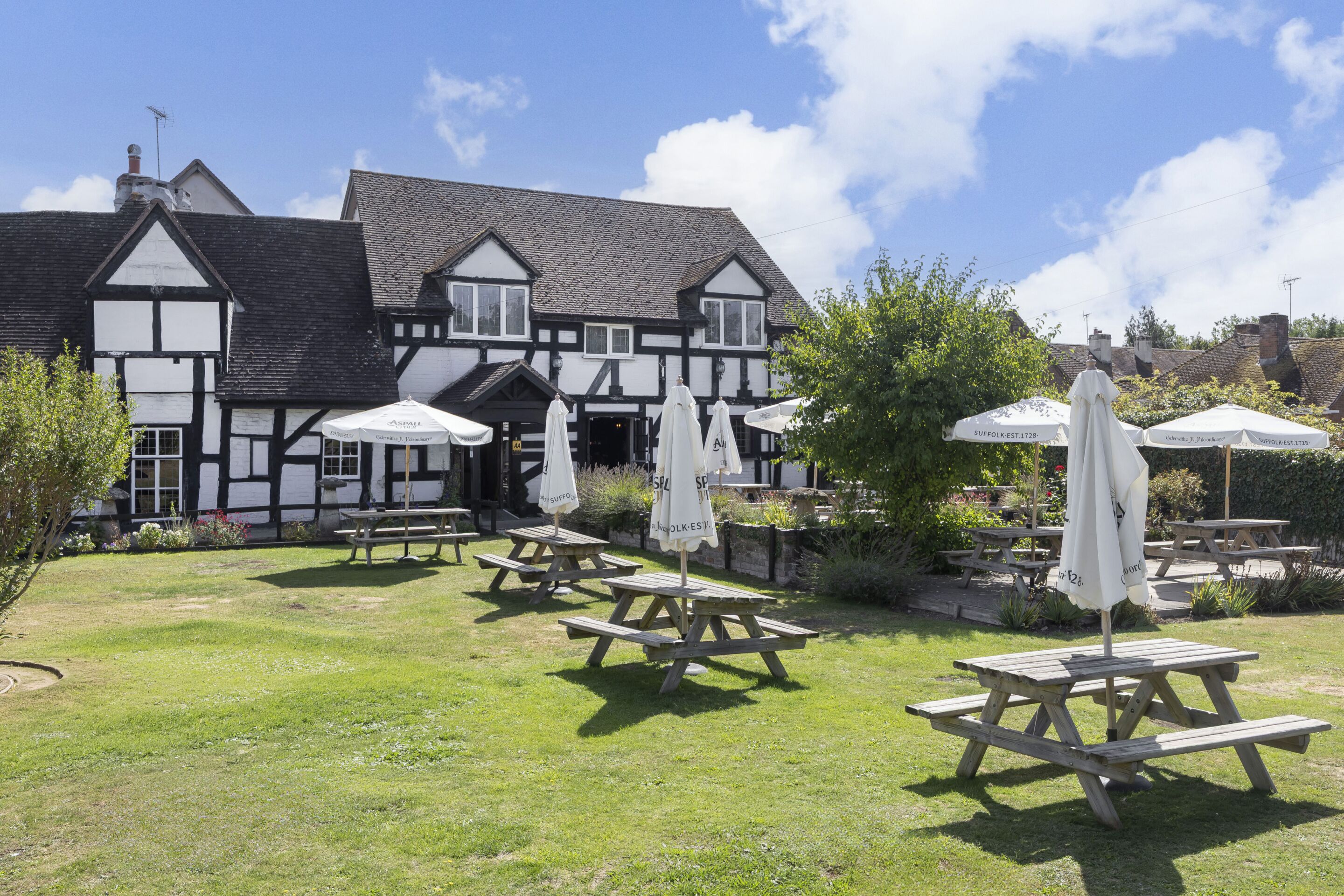 A traditional Tudor-style building with a garden patio area featuring wooden tables and white umbrellas.