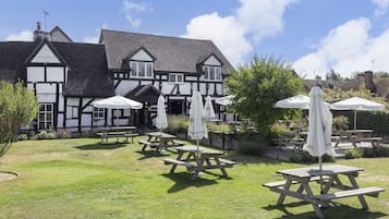 A traditional Tudor-style building with a garden patio area featuring wooden tables and white umbrellas.