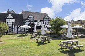 A traditional Tudor-style building with a garden patio area featuring wooden tables and white umbrellas.