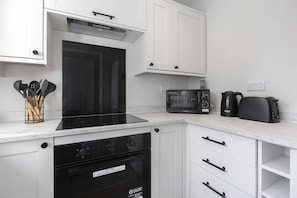 Una cocina moderna con armarios blancos, un microondas integrado, una tetera y una estufa.