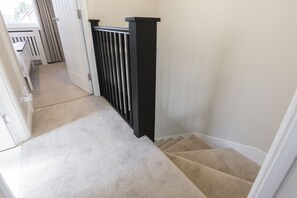 Una escalera alfombrada con barandilla negra que sube a un piso superior.