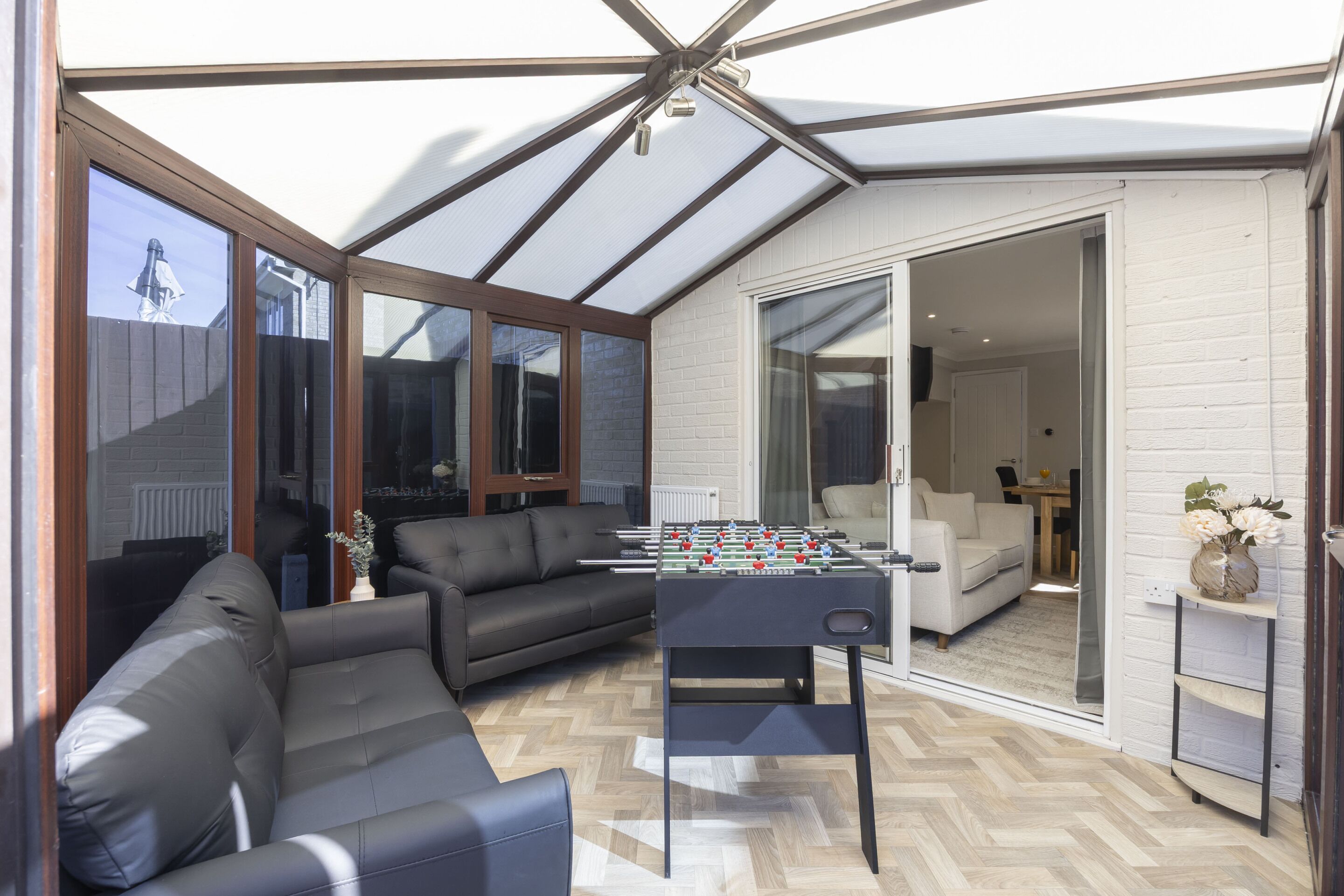 A modern living room with a foosball table, leather sofa, and a glass door leading to an adjacent room.