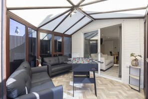 A modern living room with a foosball table, leather sofa, and a glass door leading to an adjacent room.