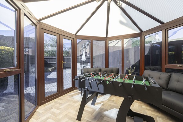 A conservatory with a foosball table and a sofa.