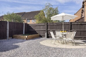 A patio with a table and chairs, a white umbrella, and a raised garden bed.