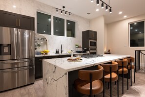 A modern kitchen with a marble island, stainless steel appliances, and a seating area with leather chairs. - 3 Luxe Homes w/ 3 Rooftops • 12BR • Sleeps 30 (Houston)
