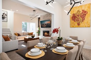 A modern living room with a dining area set for a meal. - 3 Luxe Homes w/ 3 Rooftops • 12BR • Sleeps 30 (Houston)