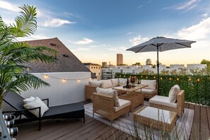 A rooftop patio with wicker furniture, string lights, and a view of the city skyline. - 3 Luxury Homes • 12BR • 3 Rooftops • Sleeps 30 (Houston)