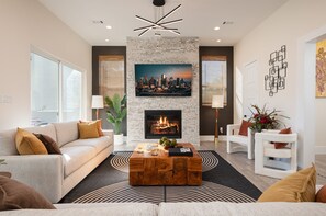 A modern living room with a fireplace, a sofa, a coffee table, and a cityscape painting above the fireplace. - 3 Luxe Homes w/ 3 Rooftops • 12BR • Sleeps 30 (Houston)