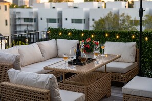 A rooftop terrace with wicker furniture, a table set with glasses and bottles, and a decorative plant. - 3 Luxe Homes w/ 3 Rooftops • 12BR • Sleeps 30 (Houston)