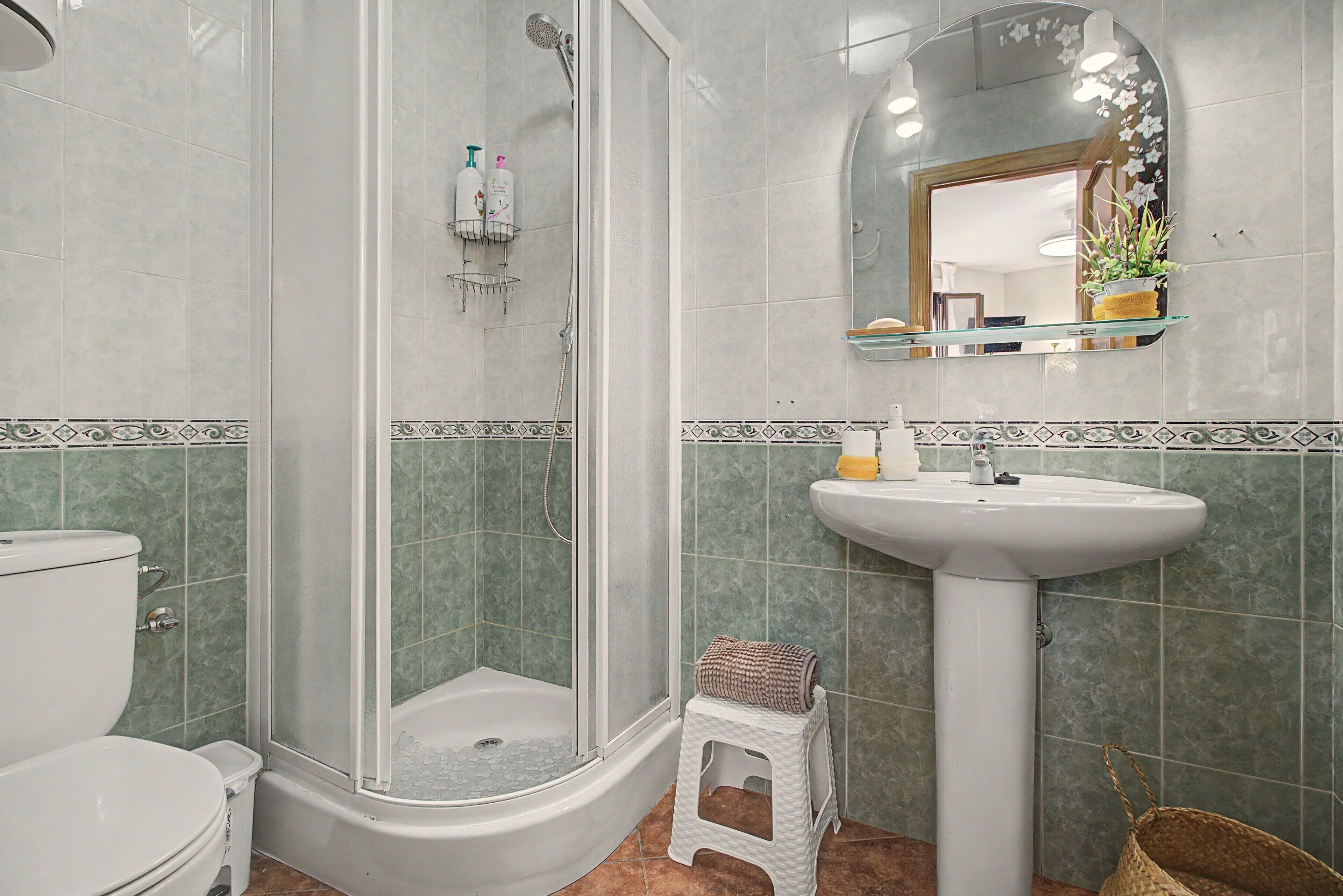 A bathroom with a glass-enclosed shower, a white pedestal sink, and a toilet.