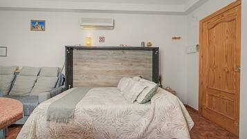 Een slaapkamer met een bed, een bank, een houten deur en een wandairconditioner.