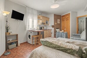 Una camera piccola e funzionale con un letto, una scrivania, una lavatrice e una televisione.