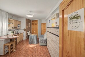 Una cucina compatta con forno a microonde, lavello e pensili in legno. C'è una zona pranzo con tavolo e sedie, e un letto con testiera. Un cartello a parete indica che si tratta di un appartamento in campagna.