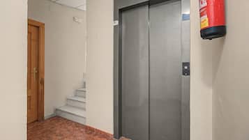 Un pasillo con puerta de madera, escalera y ascensor metálico.