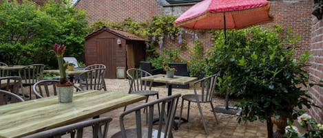 An outdoor patio area with brick walls, wooden tables, metal chairs, and a red umbrella.