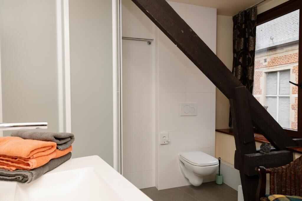 Et badeværelse med toilet, et håndklædestativ med sammenfoldede håndklæder og et vindue med gardiner.