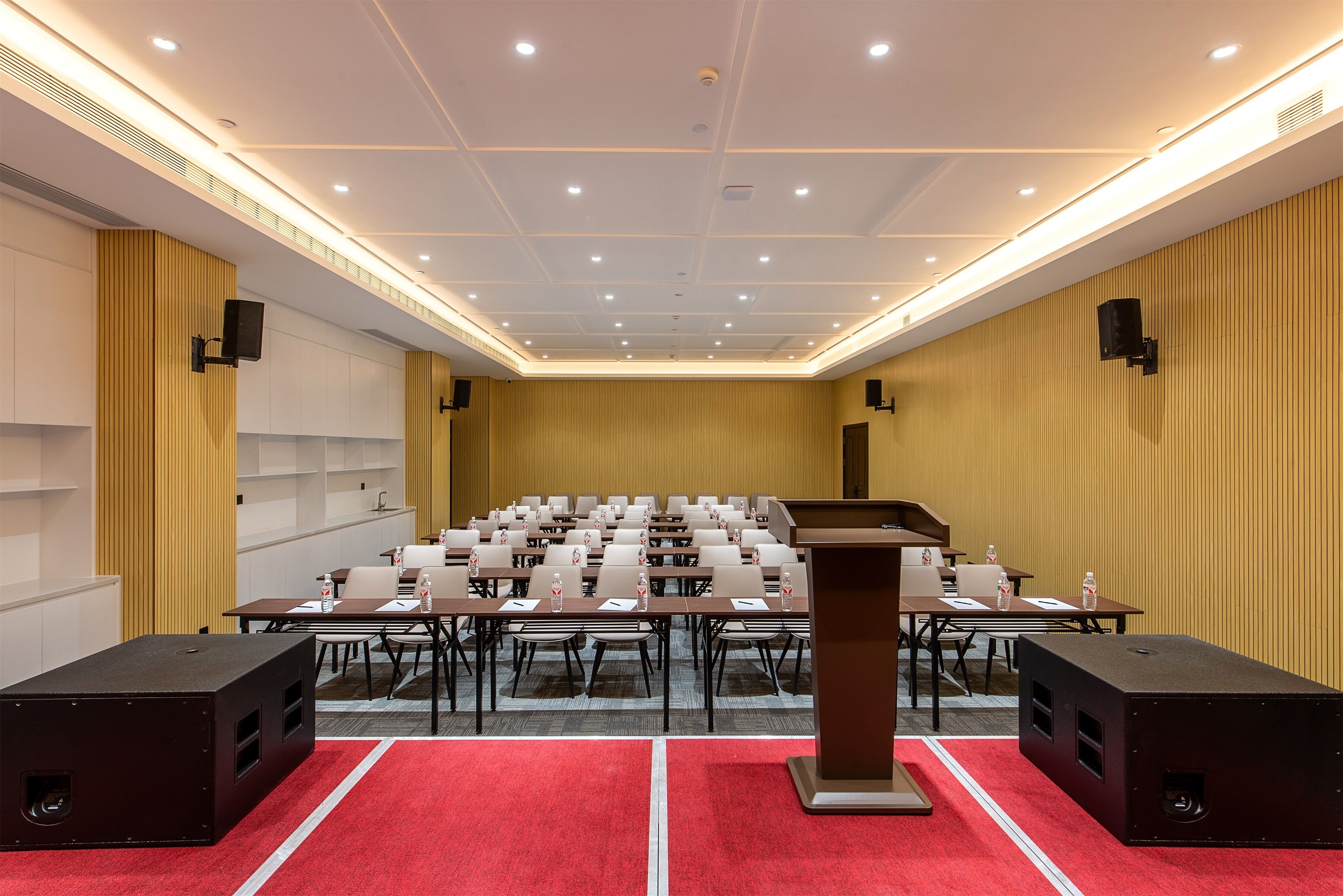 Un salón de conferencias con un atril, mesas, sillas y ponentes.
