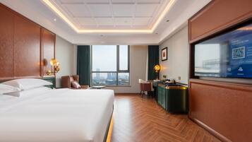 Habitación de hotel con una cama grande, un escritorio, una silla, un televisor y vistas a la ciudad.