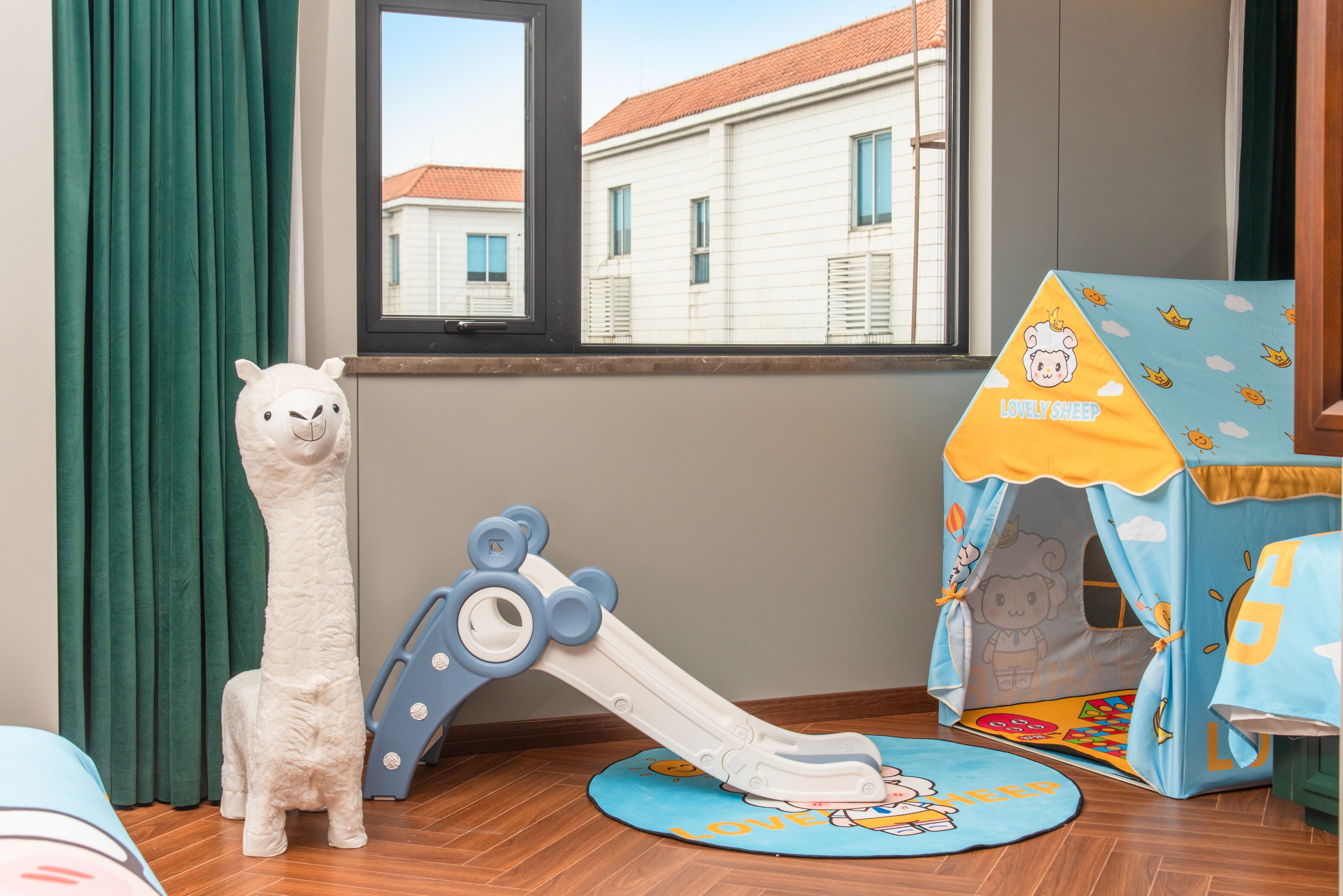 Een kamer met een raam, een knuffeltent, een speelgoedlama en een glijbaantje.