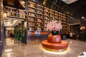 A library with bookshelves, a fireplace, and a seating area with a vase of flowers. - ELITE James Coffetel Baiyun Wanda Plaza (Guangzhou)