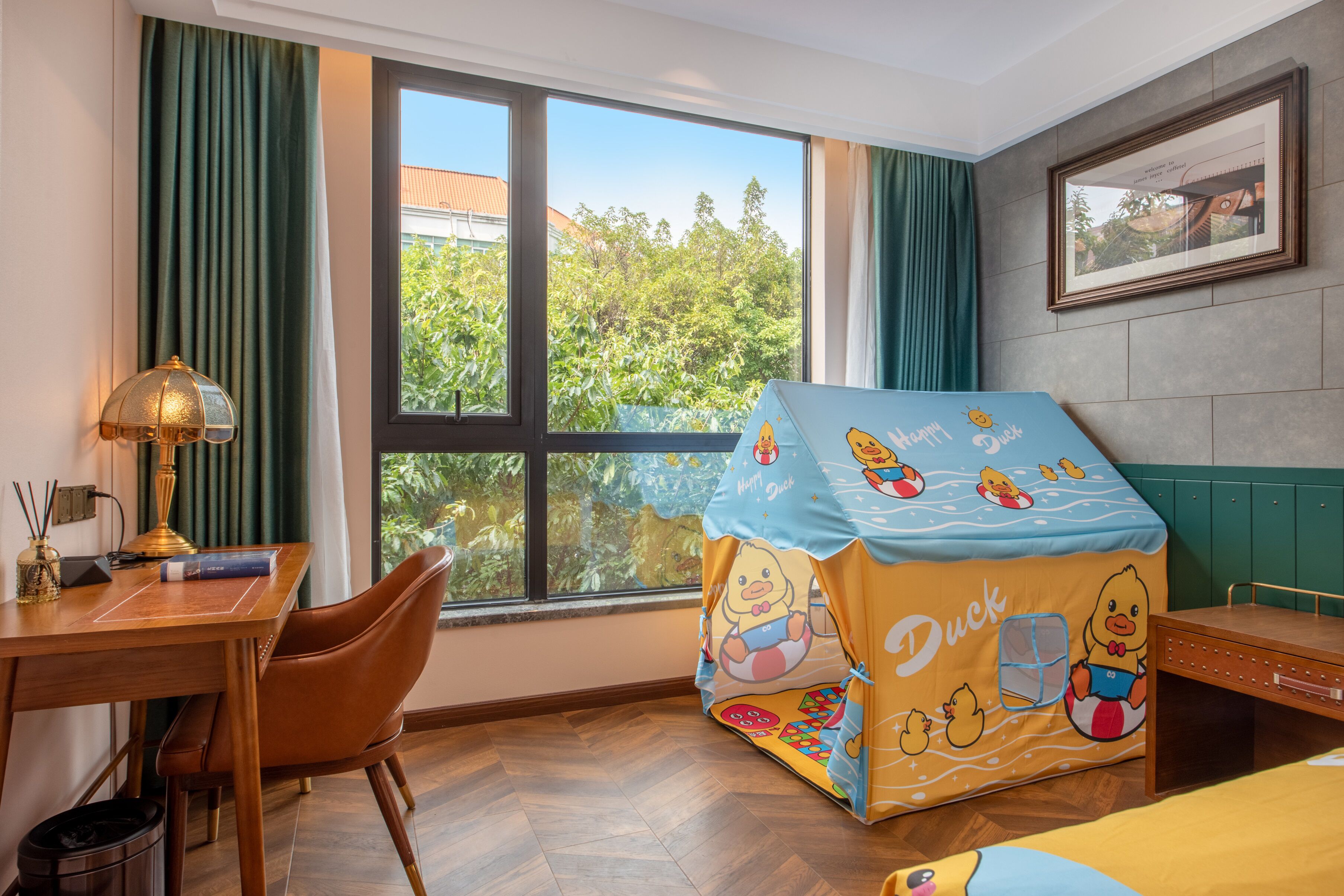 Habitación de hotel con escritorio, silla y ventana con vistas a zonas verdes.