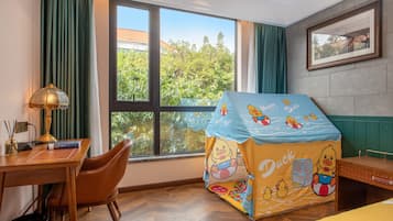 Habitación de hotel con escritorio, silla y ventana con vistas a zonas verdes.