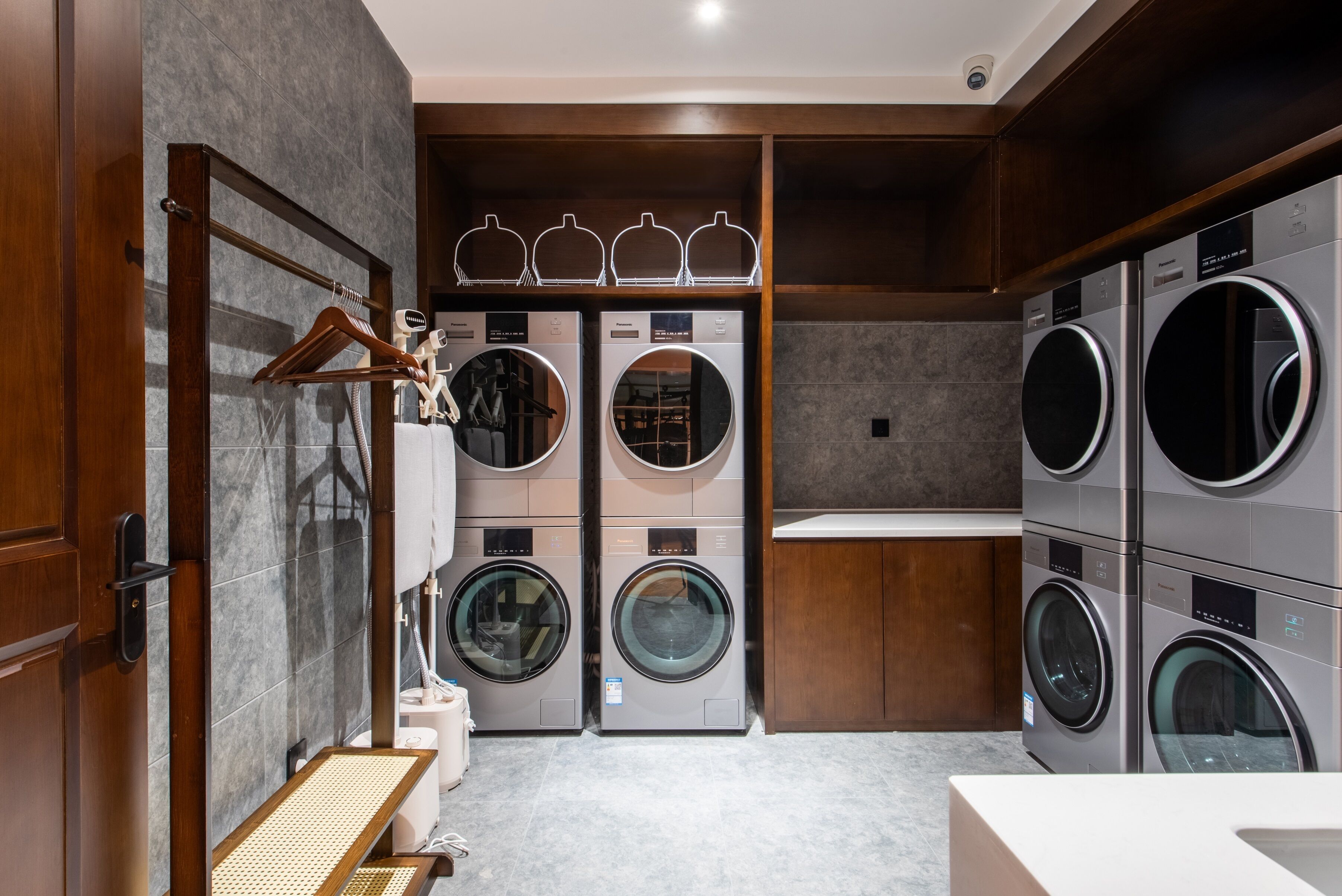 A laundry room with multiple washing machines, a drying rack, and a wooden door.