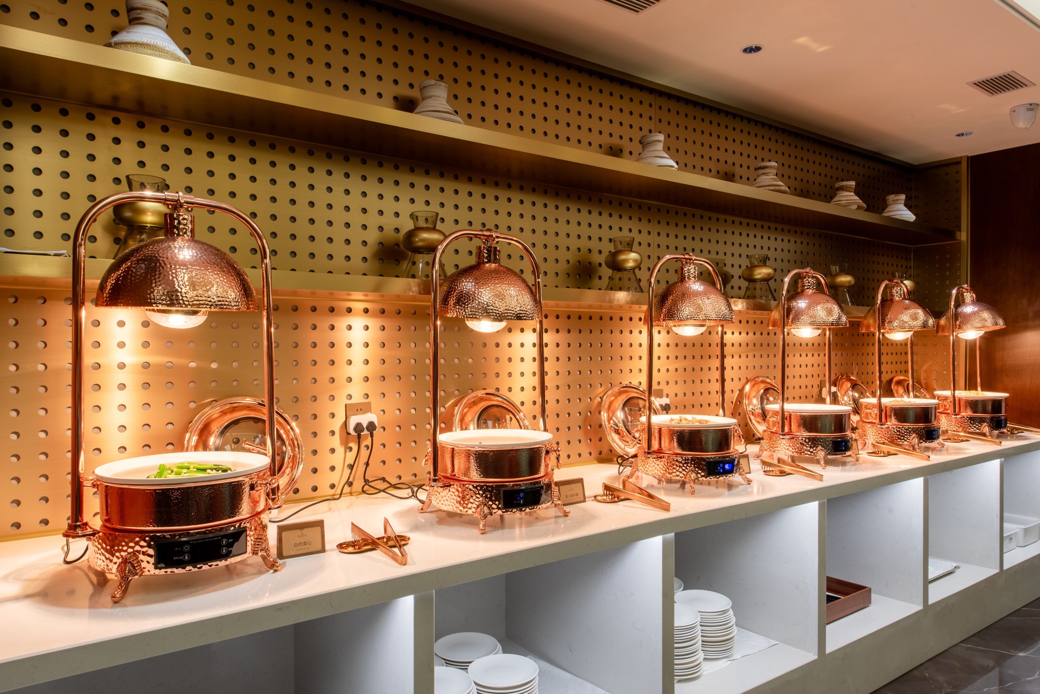 A buffet setup with copper-toned serving stations, each equipped with a pot and a spoon.
