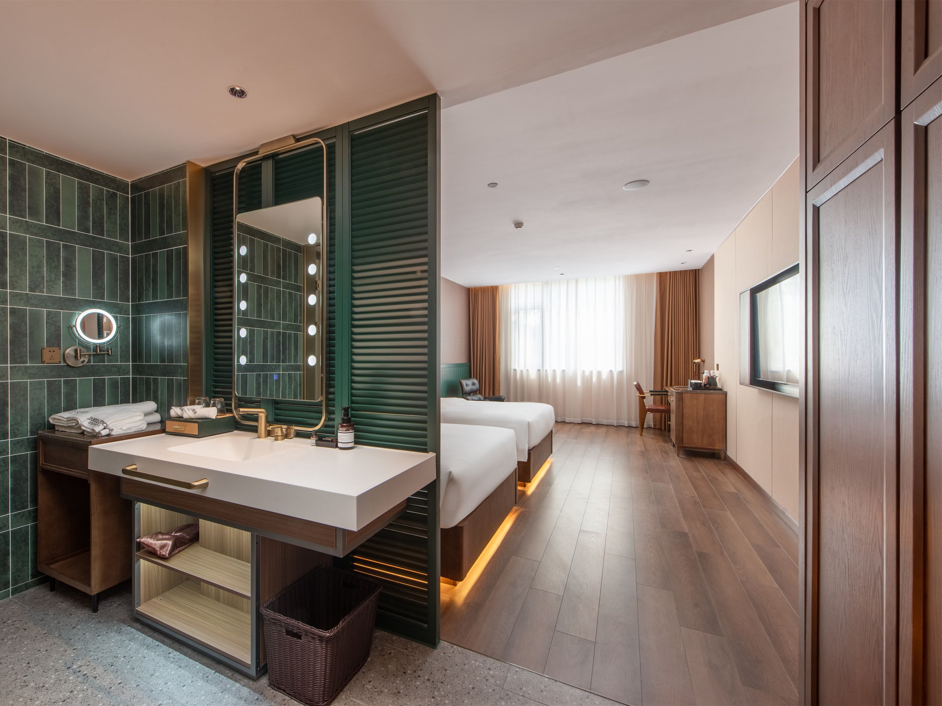 Ein Hotelzimmer mit einem großen Spiegel, einem Schminktisch mit Waschbecken, zwei Betten, einem Schreibtisch und einem Fernseher.