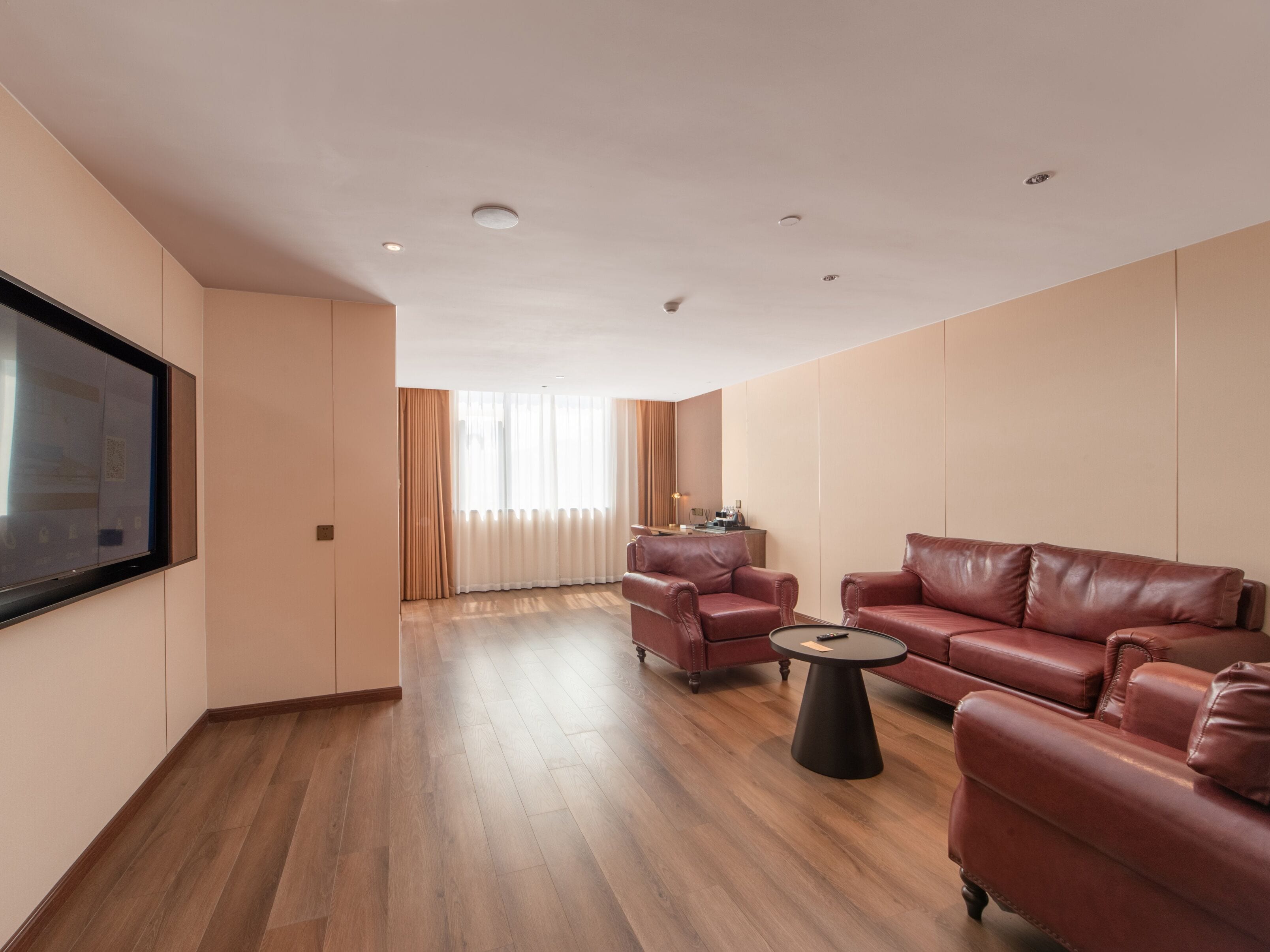 Amplia sala de estar con una televisión de pantalla plana grande montada en la pared, sofás de cuero, una mesa de centro y piso de madera.