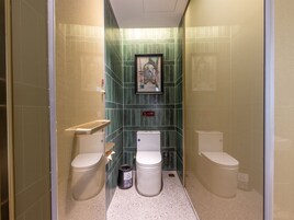 Un baño pequeño y estrecho con dos inodoros, un cubo de basura y un cuadro en la pared.