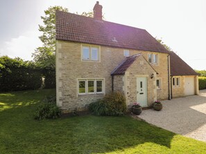 A two-story stone house with a tiled roof, a front door, and a small garden area with a gravel driveway. - The Paddocks (Chippenham)