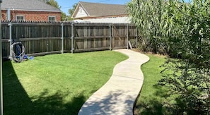 A backyard with a curved concrete pathway, a wooden fence, and a grassy lawn.