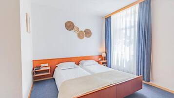 Habitación de hotel con cama doble, mesitas de noche, lámpara y ventana con cortinas.