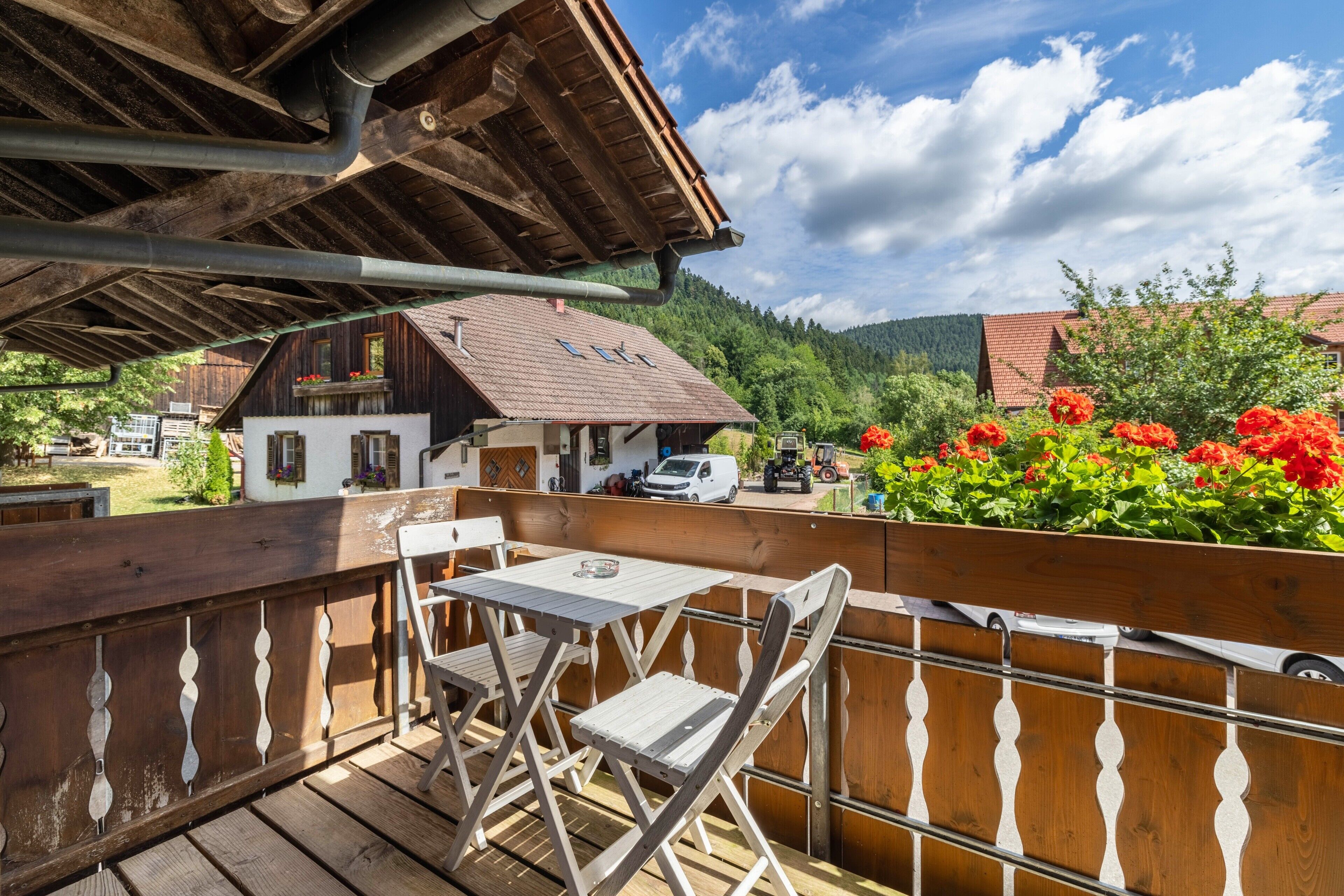 Una terraza de madera con una mesa y sillas, con vistas a un pueblo de edificios tradicionales y un telón de fondo montañoso.