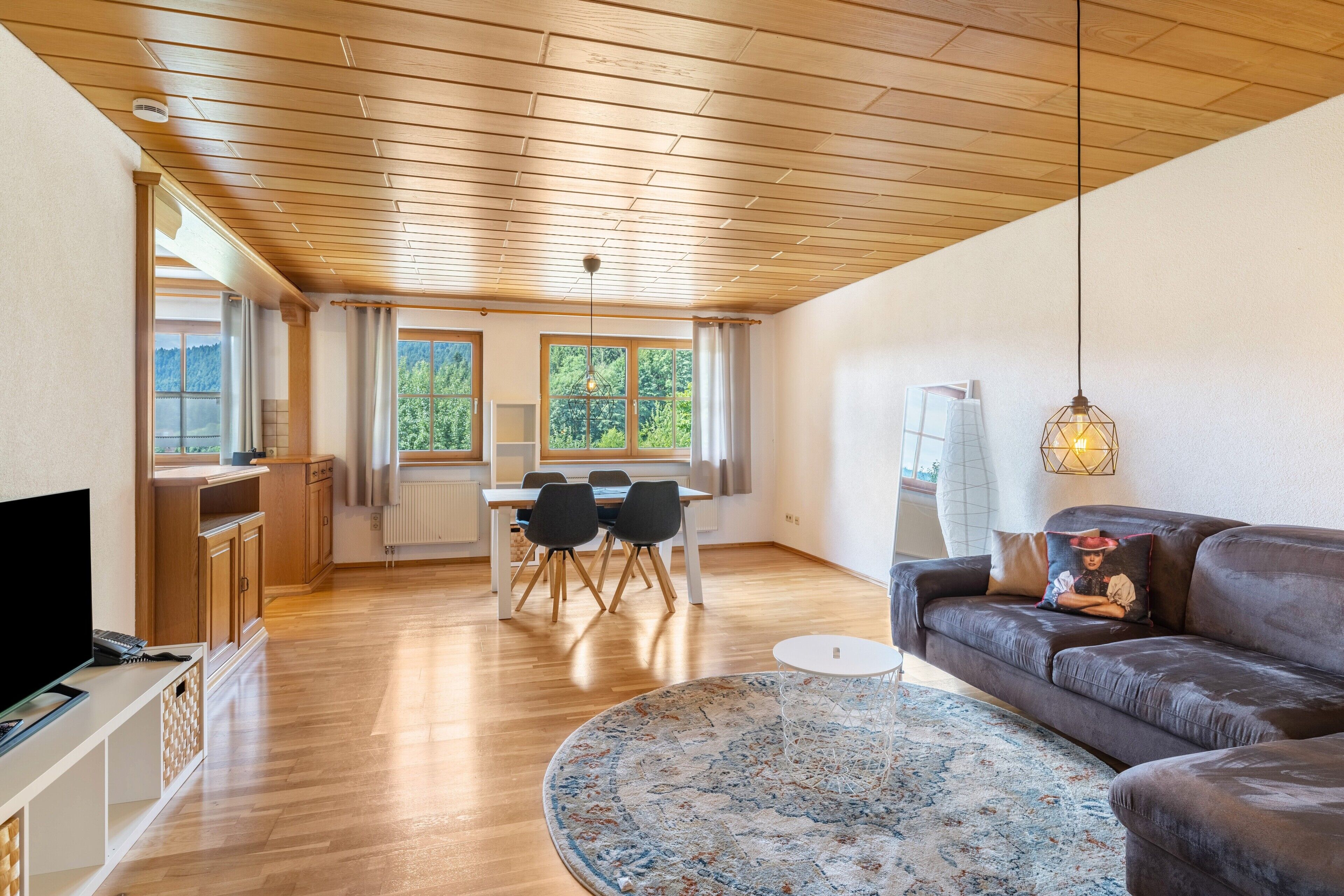 Uma sala de estar moderna com teto de madeira, um sofá, mesa de centro redonda e um espaço de jantar com mesa e cadeiras.