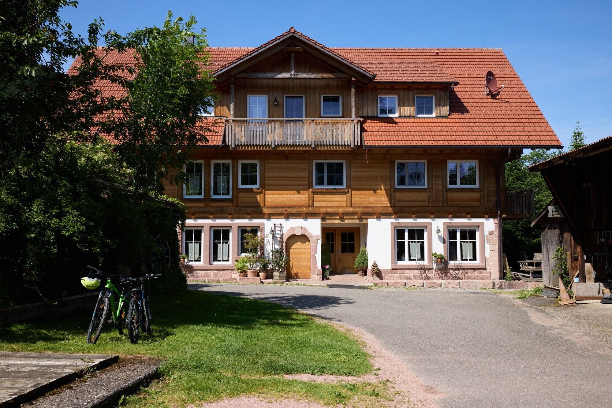 A two-story wooden house with a balcony, a driveway, and a bicycle parked outside.