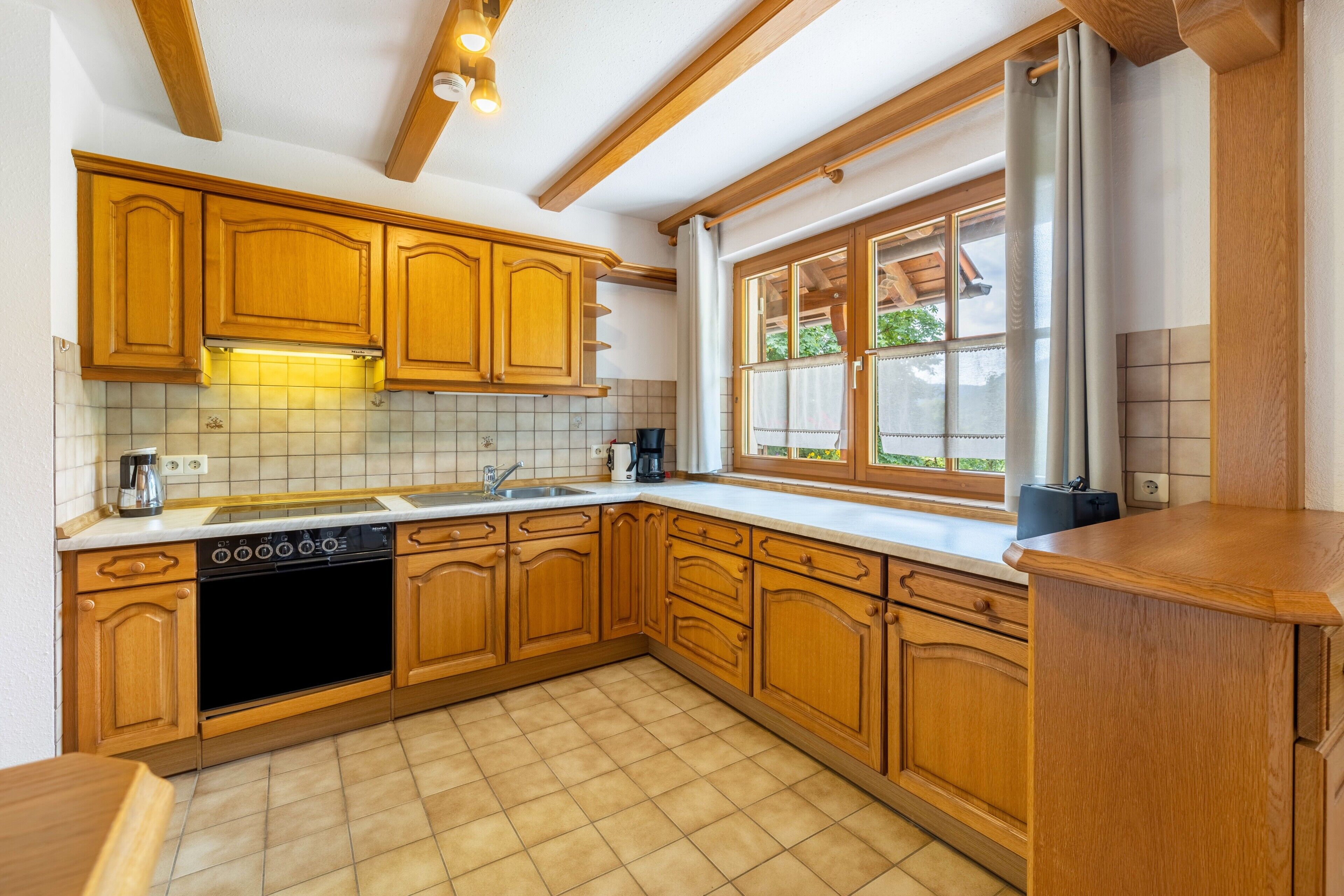 A kitchen with wooden cabinets, a dishwasher, and a window with curtains.