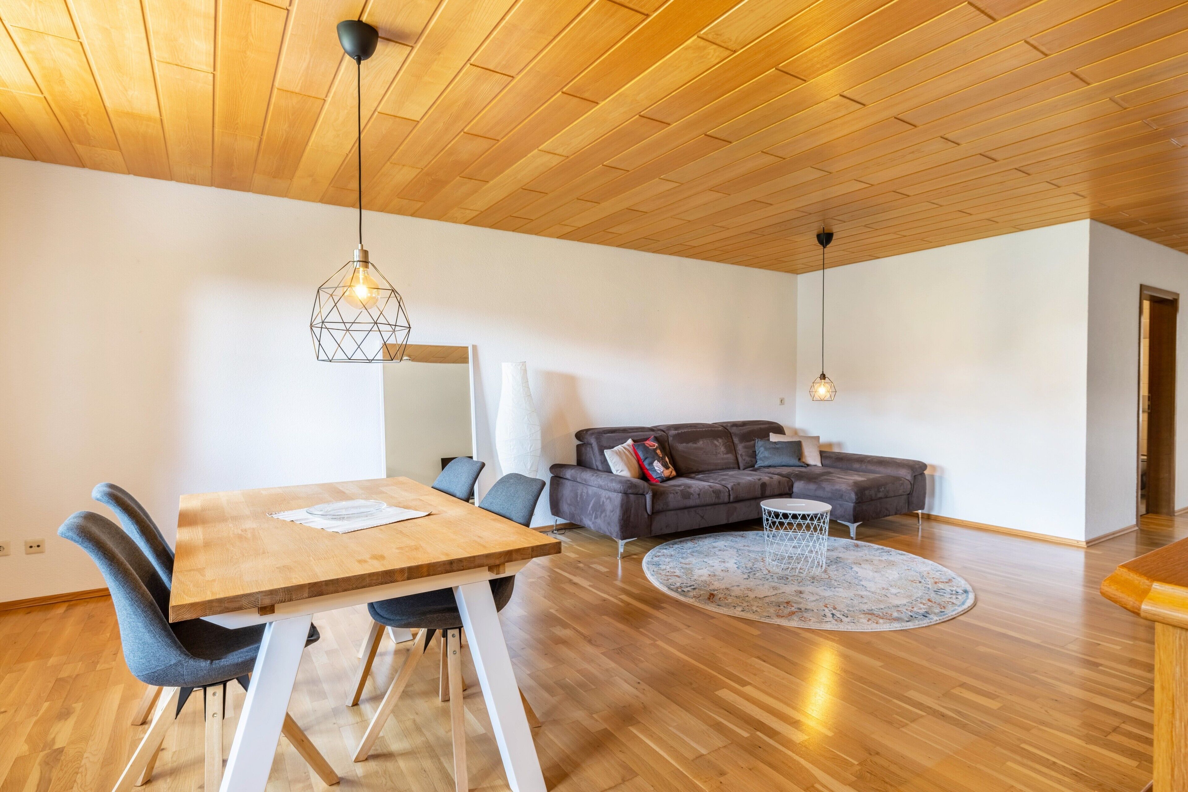 Amplia sala de estar con techo de madera, una mesa de comedor con sillas, un sofá y dos lámparas colgantes.