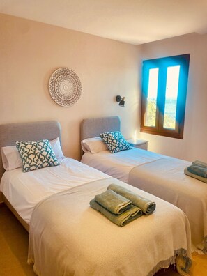A room with two beds, a wall-mounted decorative plate, a bedside lamp, and a window with daylight.