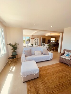 A spacious living area with a sofa, ottoman, and a dining area in the background.
