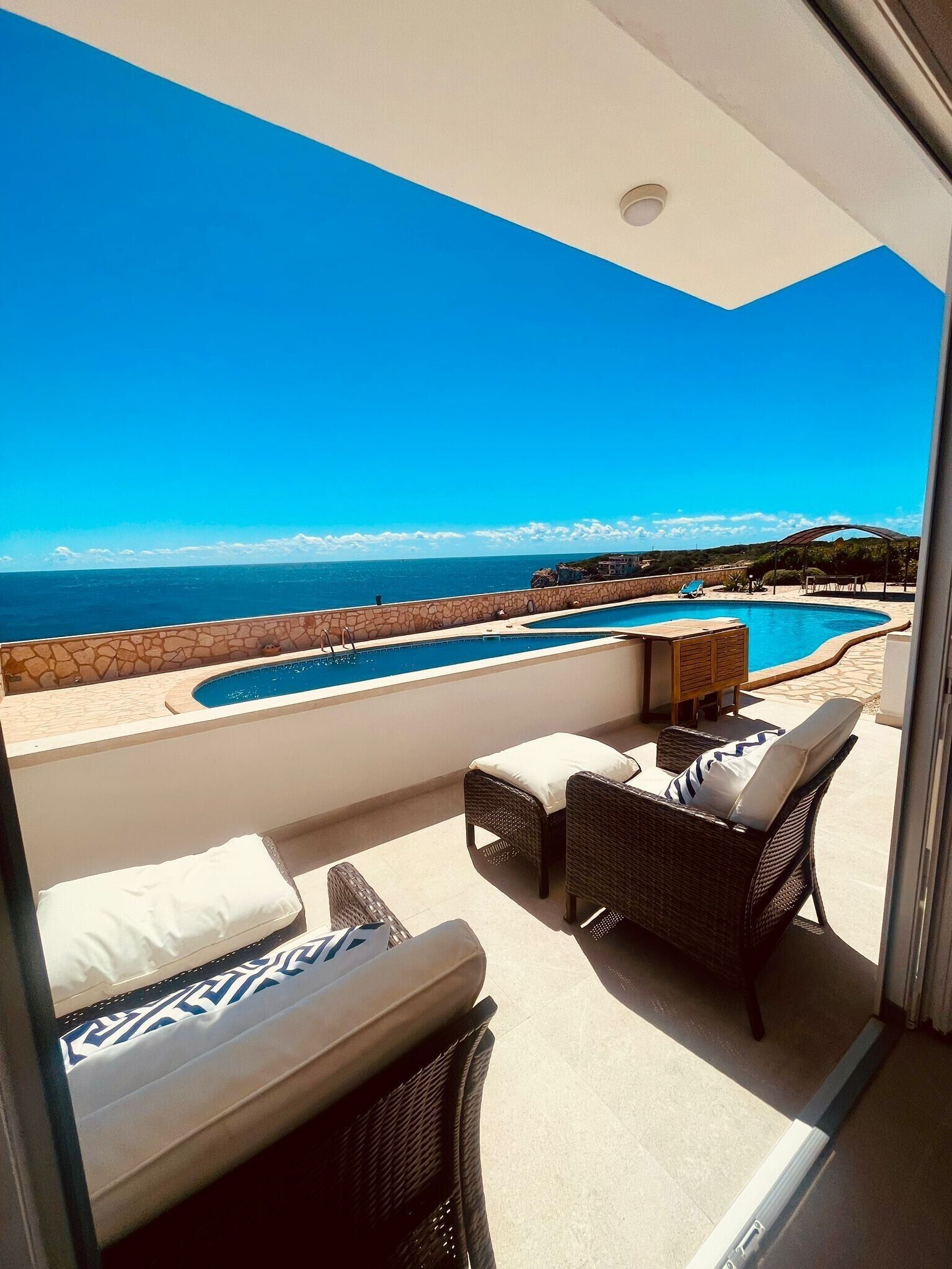 A balcony with a view of the sea, a swimming pool, and outdoor furniture.