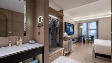 Una habitación de hotel moderna con una cama grande, un baño con tocador, un televisor y una zona de estar con una mesa y sillas.