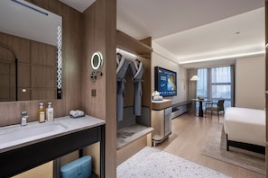 A modern hotel room with a large bed, a bathroom with a vanity, a television, and a seating area with a table and chairs. - Manxin Hotel Anzhen Qiao Metro Station (Beijing)