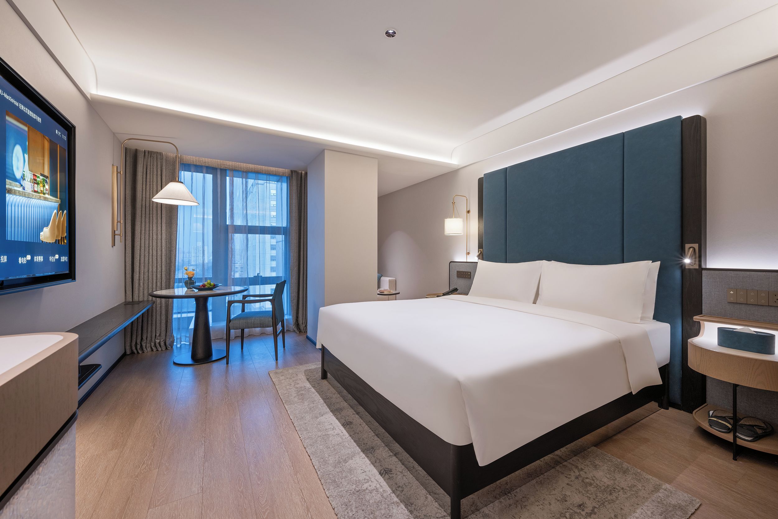 A modern hotel room with a large bed, a desk, and a television.