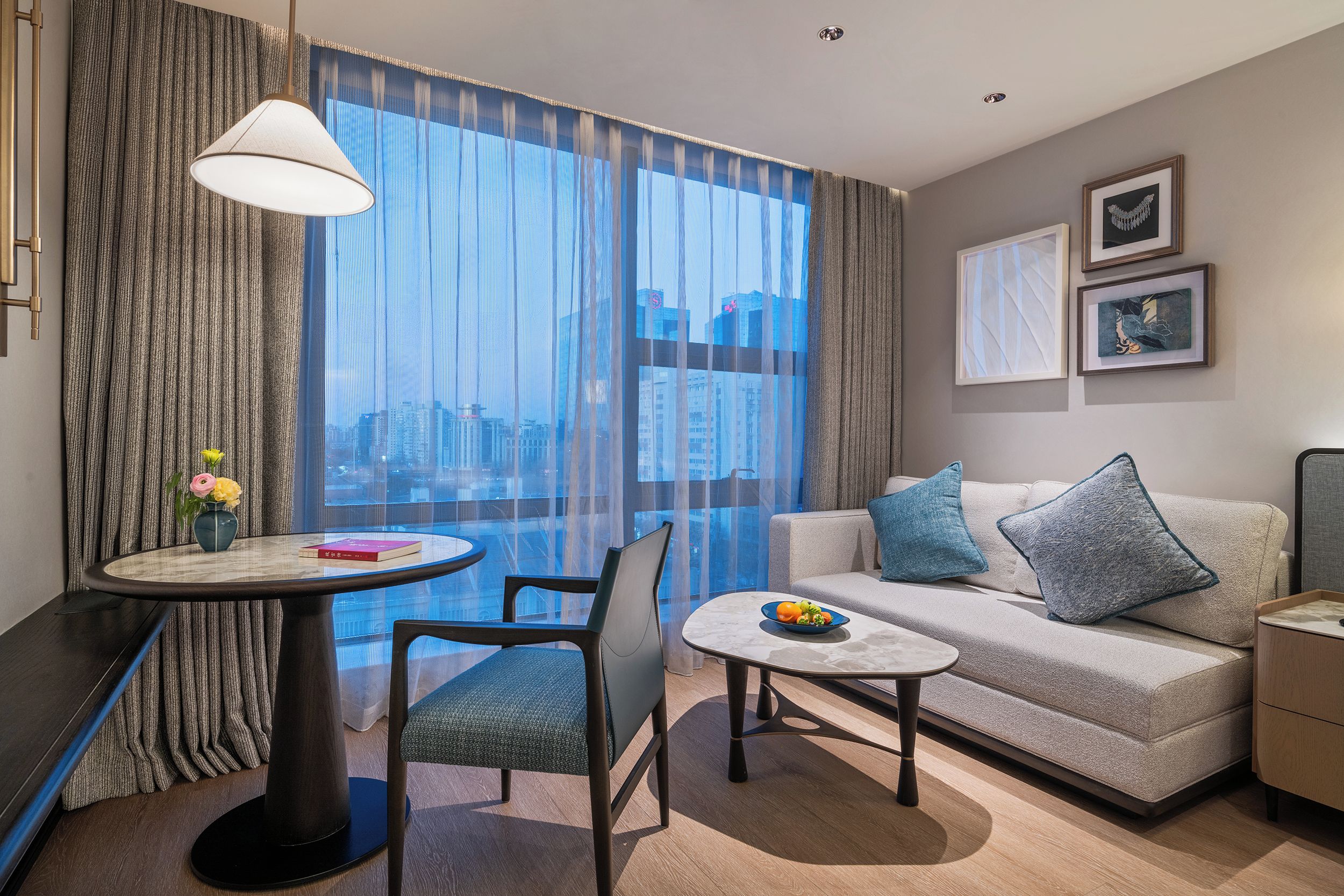 A modern hotel room with a balcony, a sofa, a dining table, and a chair.