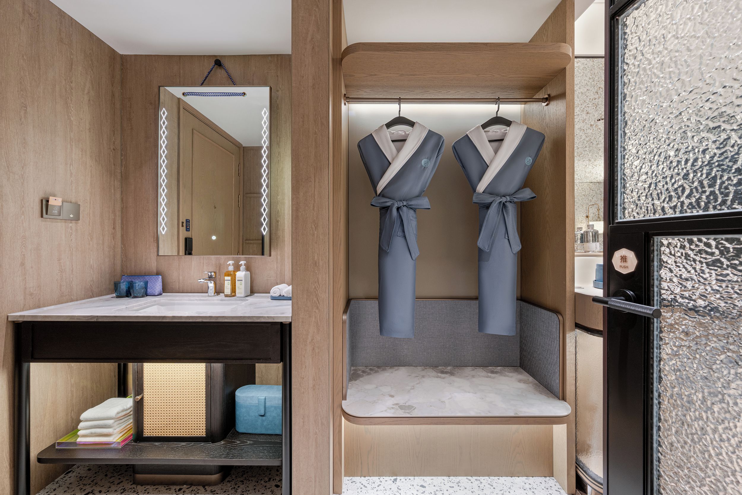 A modern bathroom with a wooden vanity, a mirror, and two robes hanging on hooks.