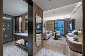 Quarto de hotel moderno com uma cama grande, área de estar com cafeteira e televisão na parede.